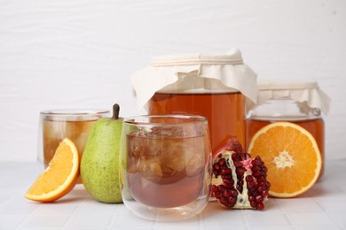 Tasty kombucha with ice cubes and fresh fruits on white tiled table