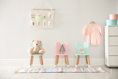 Photo of Cute toys on chairs with bunny ears near white wall indoors. Children's room interior