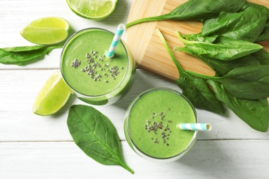 Glasses of healthy green smoothie with fresh spinach on white wooden table, flat lay