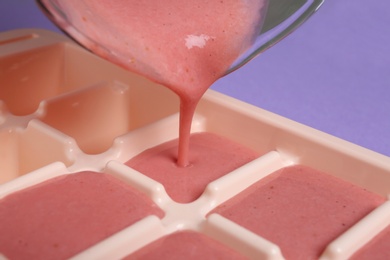 Photo of Pouring smoothie into ice cube tray on table, closeup