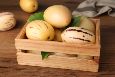 Photo of Fresh ripe pepino melons with green leaves in crate on wooden table