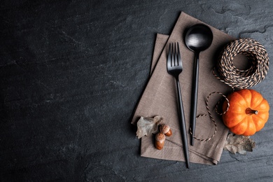 Cutlery, pumpkin and rope on black slate background, flat lay with space for text. Table setting elements