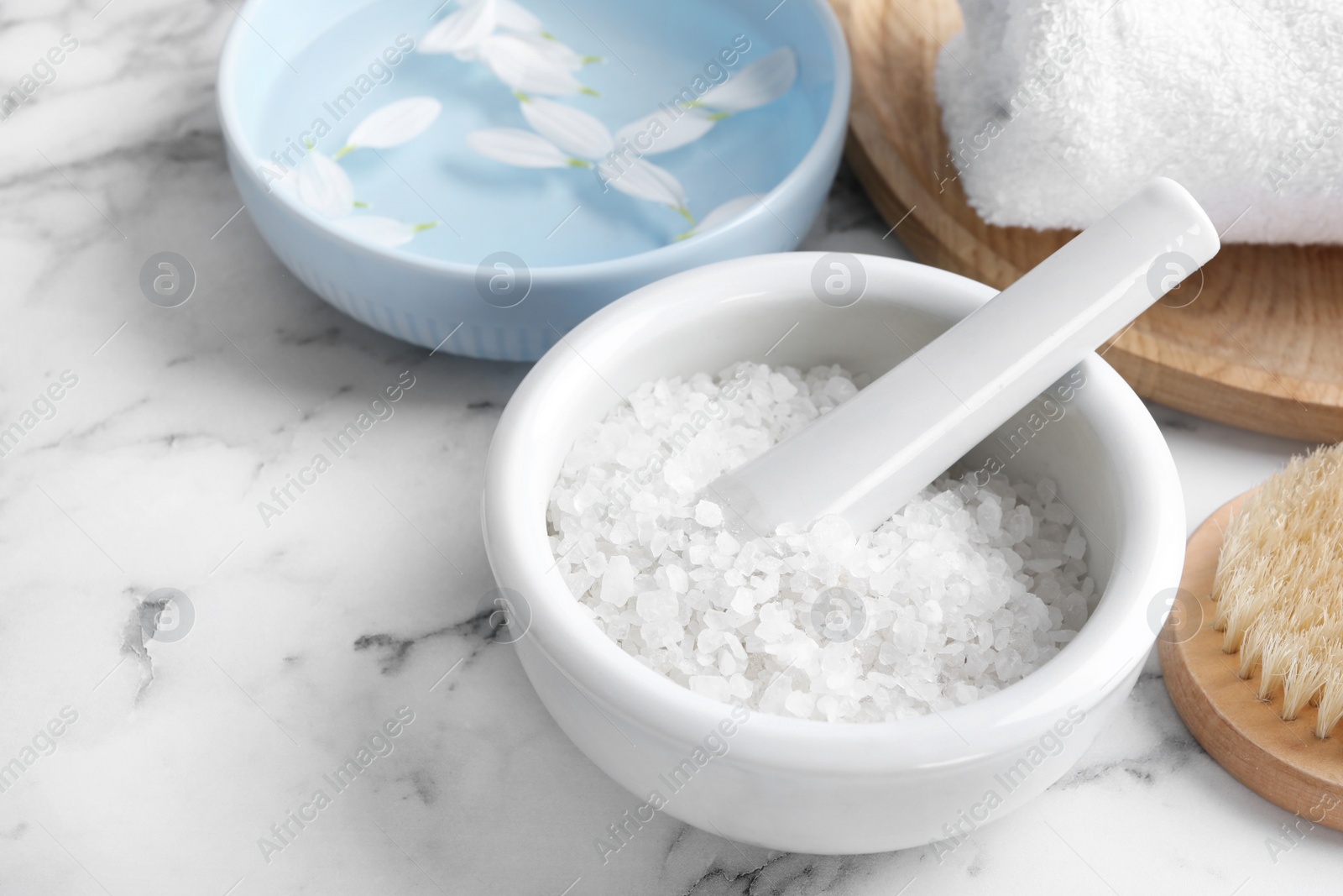 Photo of Mortar and pestle with white sea salt for spa scrubbing procedure on marble table