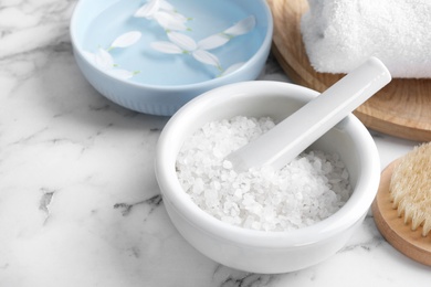 Mortar and pestle with white sea salt for spa scrubbing procedure on marble table