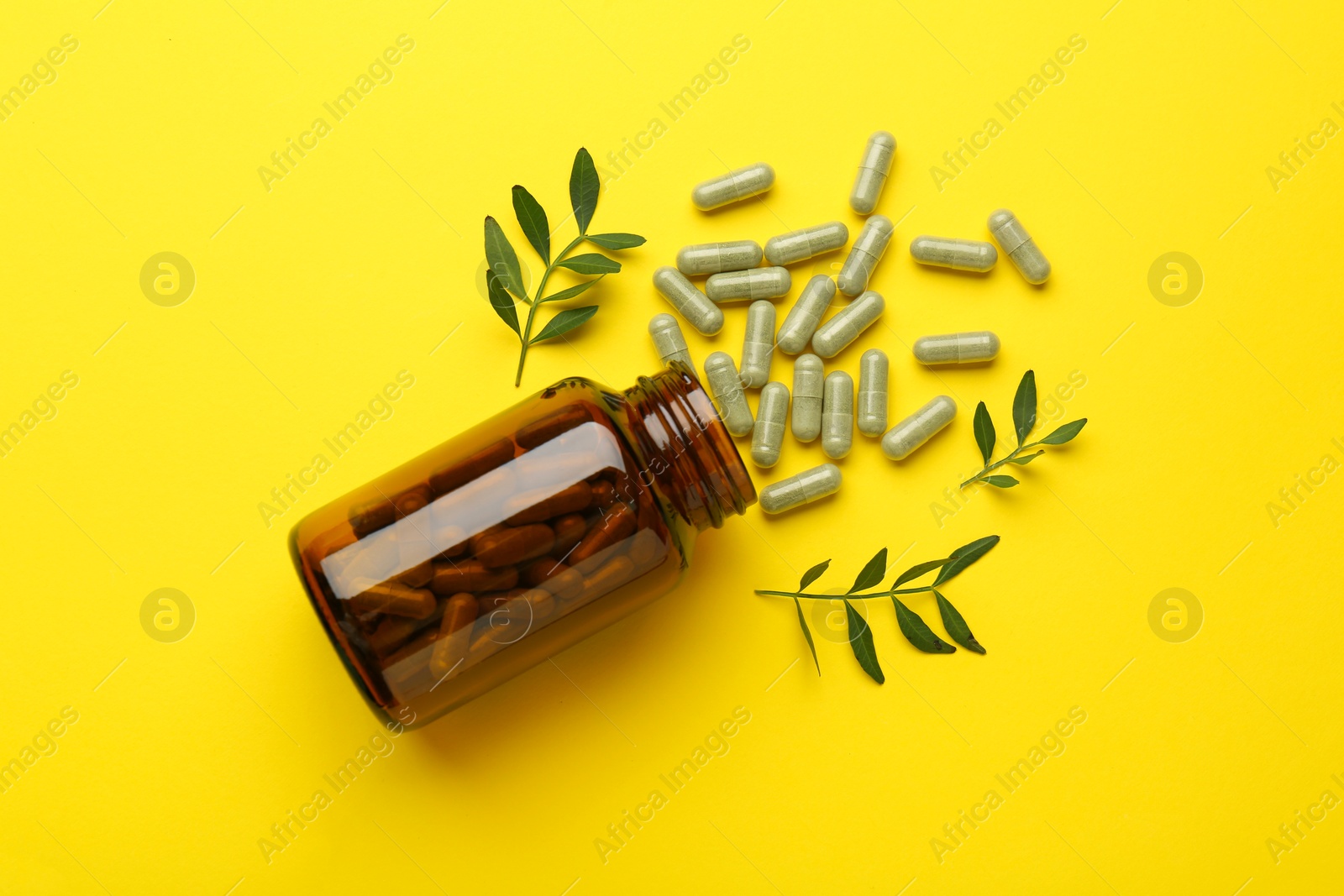 Photo of Vitamin pills, branches and bottle on yellow background, flat lay