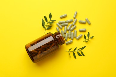 Photo of Vitamin pills, branches and bottle on yellow background, flat lay