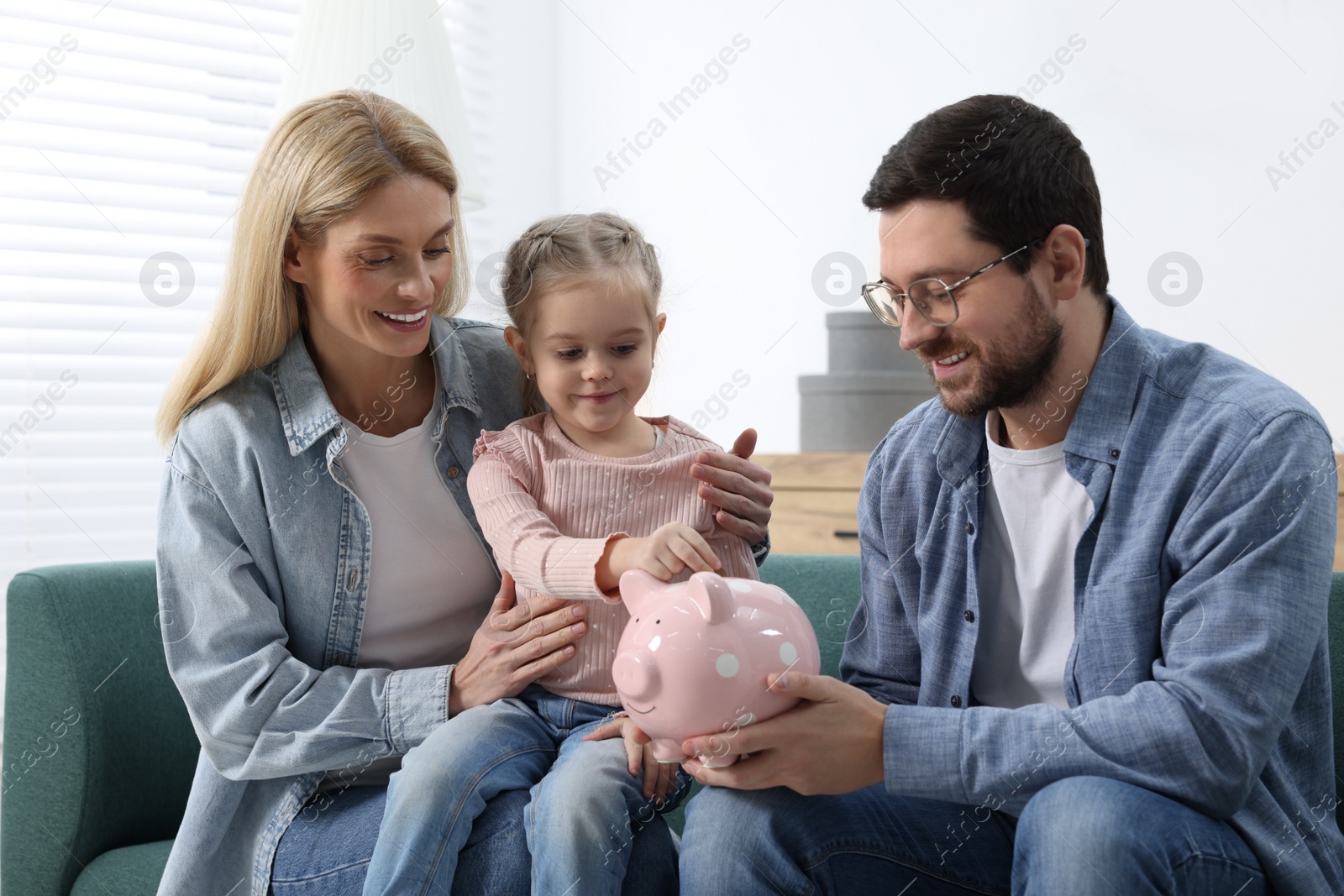 Photo of Planning budget together. Little girl with her parents putting coin into piggybank at home