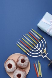 Flat lay composition with Hanukkah menorah and donuts on blue background, space for text