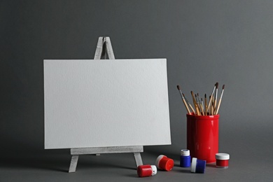 Photo of Wooden easel with blank canvas board and painting tools for children on dark background. Space for text