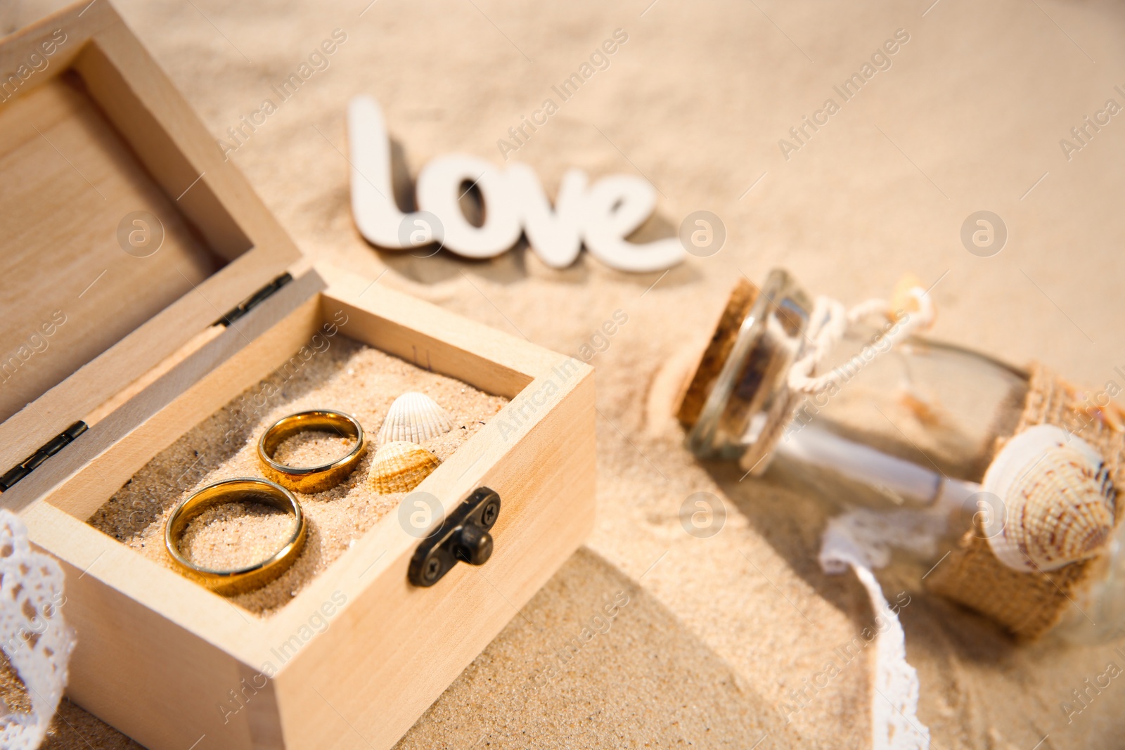 Photo of Wooden box with gold wedding rings on sandy beach, closeup