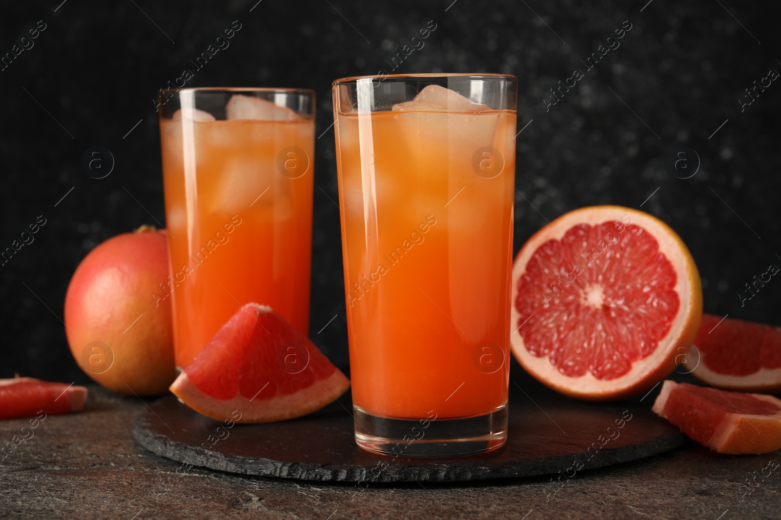 Photo of Tasty grapefruit drink with ice in glasses and fresh fruits on dark textured table