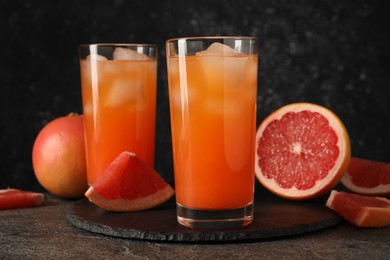 Tasty grapefruit drink with ice in glasses and fresh fruits on dark textured table