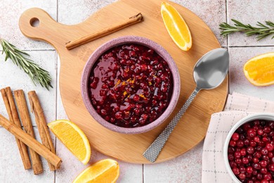 Tasty cranberry sauce in bowl and ingredients on white tiled table, flat lay