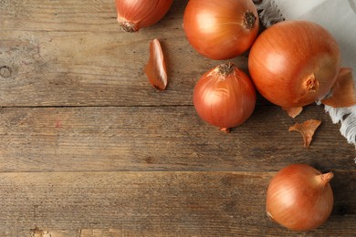 Photo of Ripe yellow onion bulbs on wooden table, flat lay. Space for text