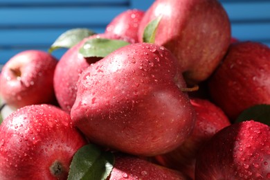 Photo of Ripe red apples with water drops and green leaves on blue background, closeup