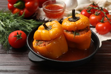 Photo of Tasty stuffed peppers in pan and products on wooden table, closeup