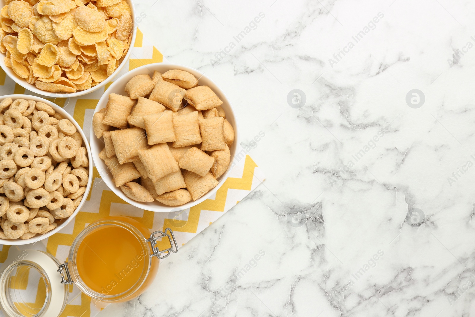 Photo of Different breakfast cereals and honey on white marble table, flat lay. Space for text