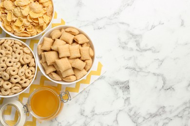 Different breakfast cereals and honey on white marble table, flat lay. Space for text