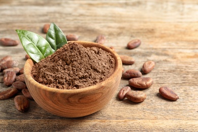 Photo of Bowl with cocoa powder on wooden table, space for text