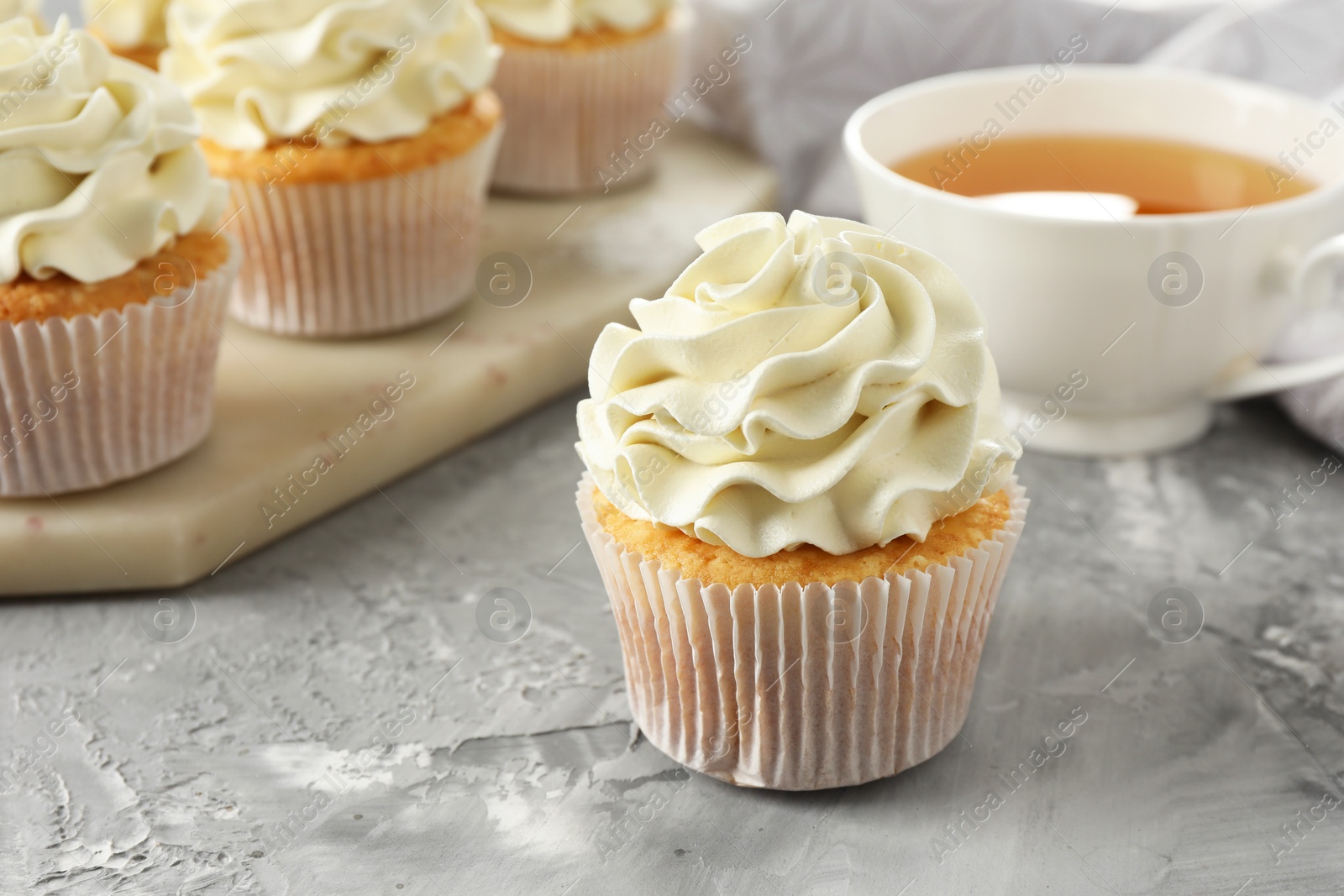 Photo of Tasty cupcakes with vanilla cream on grey table, closeup