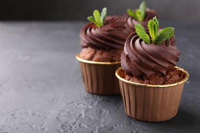 Photo of Delicious chocolate cupcakes with mint on black textured table, closeup. Space for text