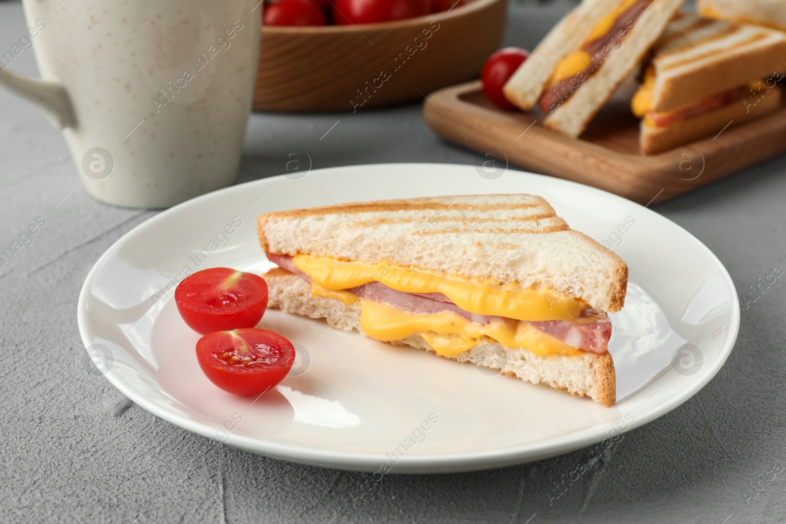 Photo of Tasty sandwich with ham, melted cheese and tomatoes on grey textured table, closeup