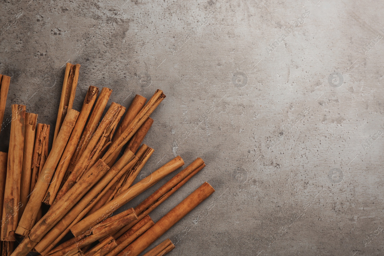 Photo of Aromatic cinnamon sticks on grey stone table, flat lay. Space for text