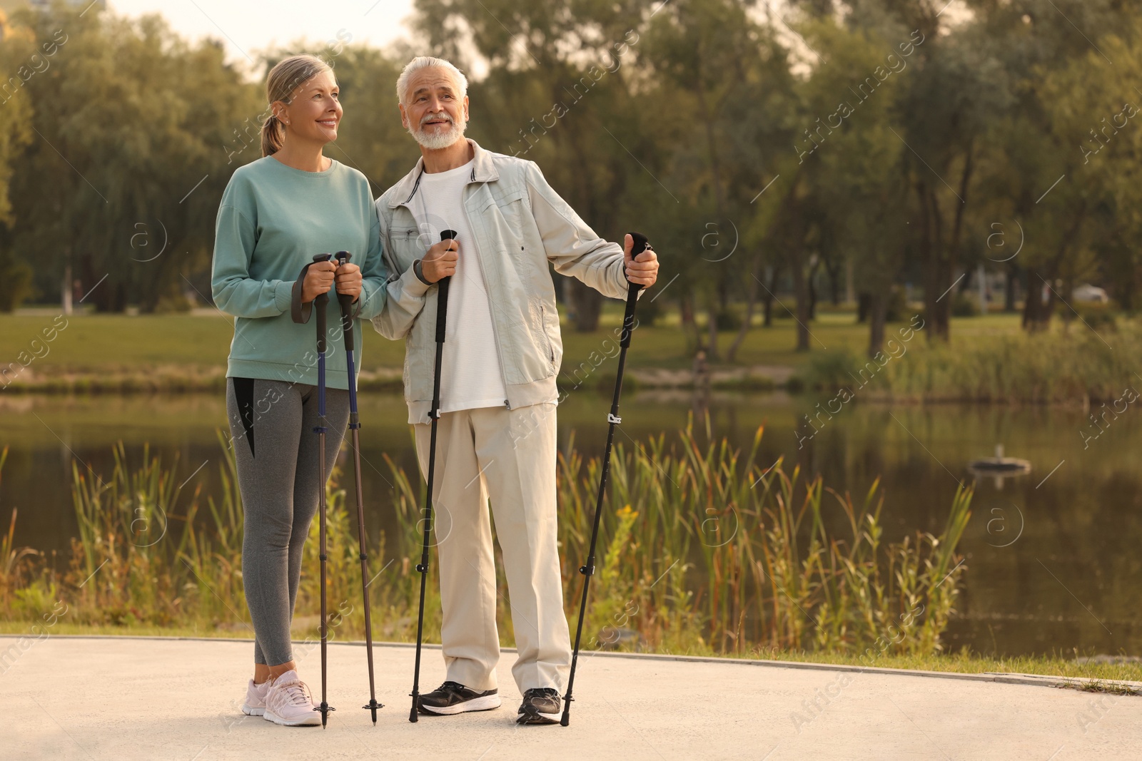 Photo of Senior man and woman with Nordic walking poles outdoors, space for text