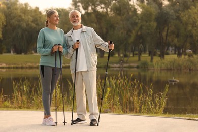 Senior man and woman with Nordic walking poles outdoors, space for text