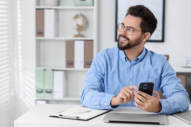 Photo of Happy young man using smartphone at white table in office, space for text