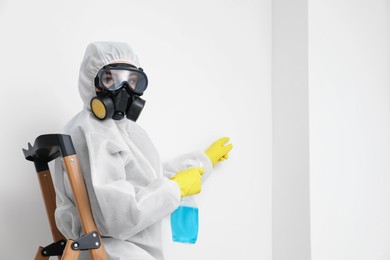 Photo of Woman in protective suit cleaning mold with sprayer on wall indoors