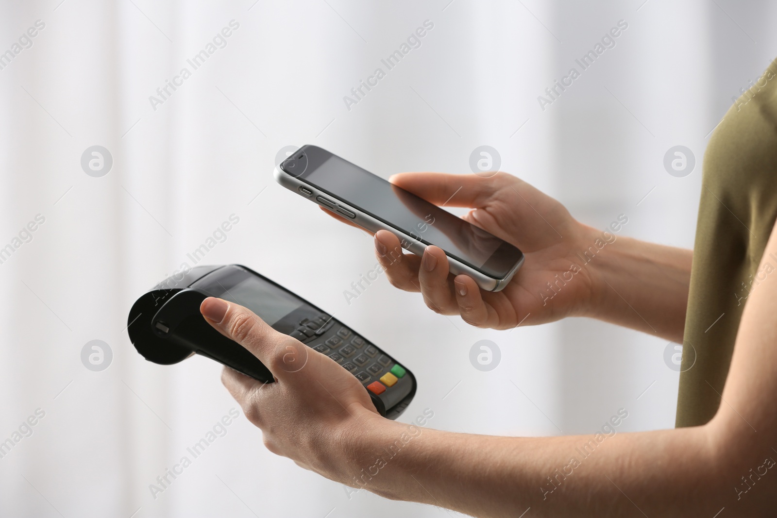 Photo of Woman using modern payment terminal with mobile phone indoors, closeup