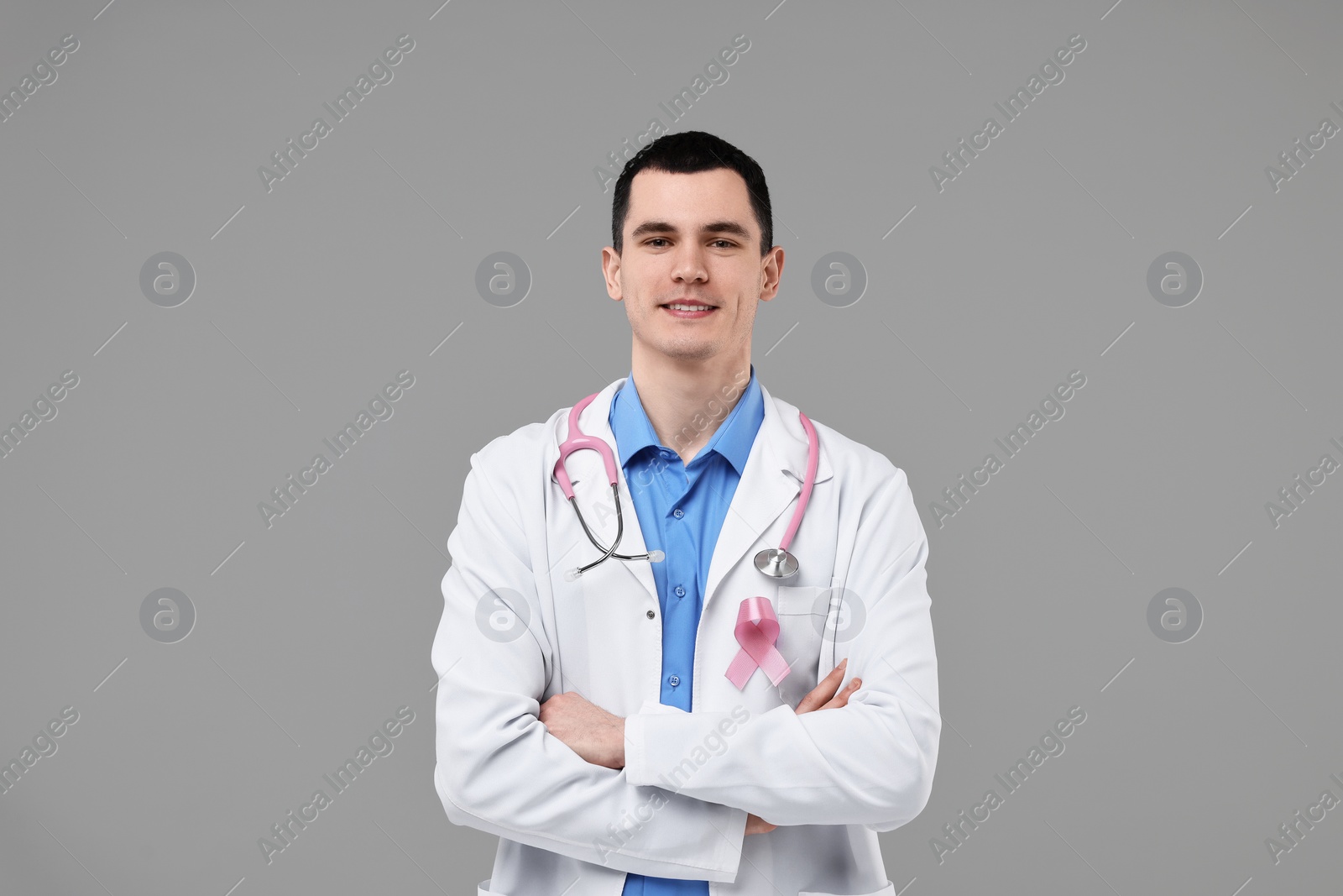 Photo of Portrait of smiling mammologist with pink ribbon and stethoscope on grey background. Breast cancer awareness