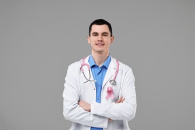 Portrait of smiling mammologist with pink ribbon and stethoscope on grey background. Breast cancer awareness