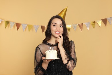 Coming of age party - 21st birthday. Smiling woman holding delicious cake with number shaped candles on beige background