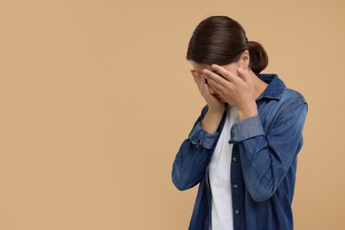 Photo of Resentful woman covering face with hands on beige background, space for text