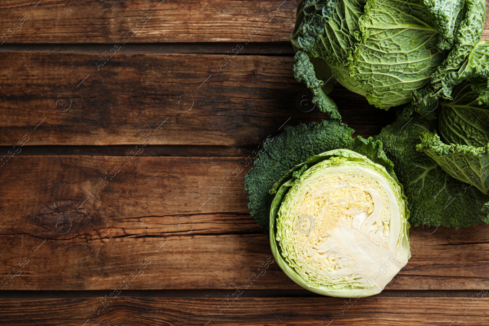 Photo of Whole and cut fresh ripe savoy cabbages on wooden table, flat lay. Space for text