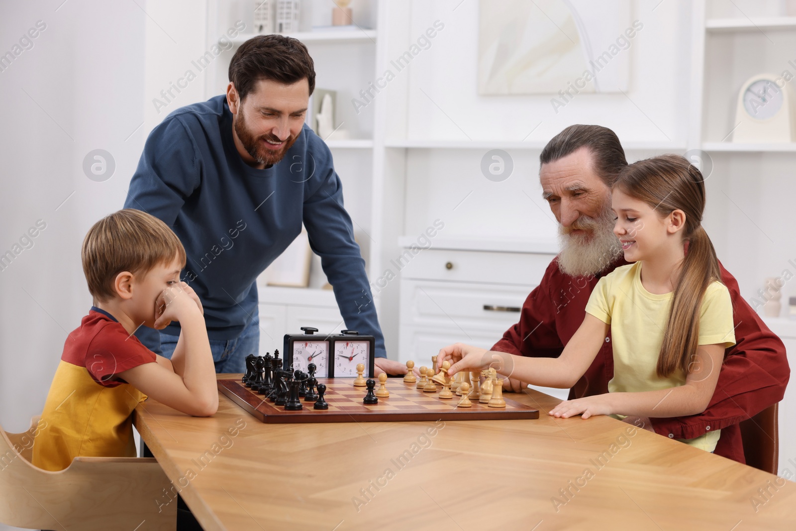 Photo of Family playing chess together at table in room