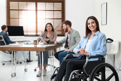 Photo of Young woman in wheelchair with colleagues at office