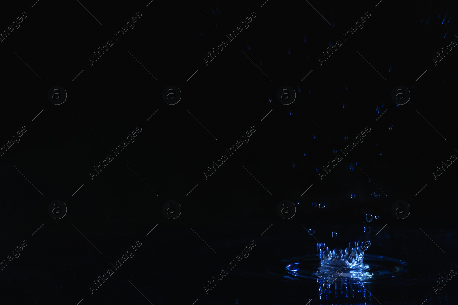 Photo of Rain drop falling down into puddle on dark background, space for text