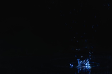 Photo of Rain drop falling down into puddle on dark background, space for text