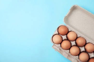 Photo of Raw chicken eggs in carton on color background, top view. Space for text