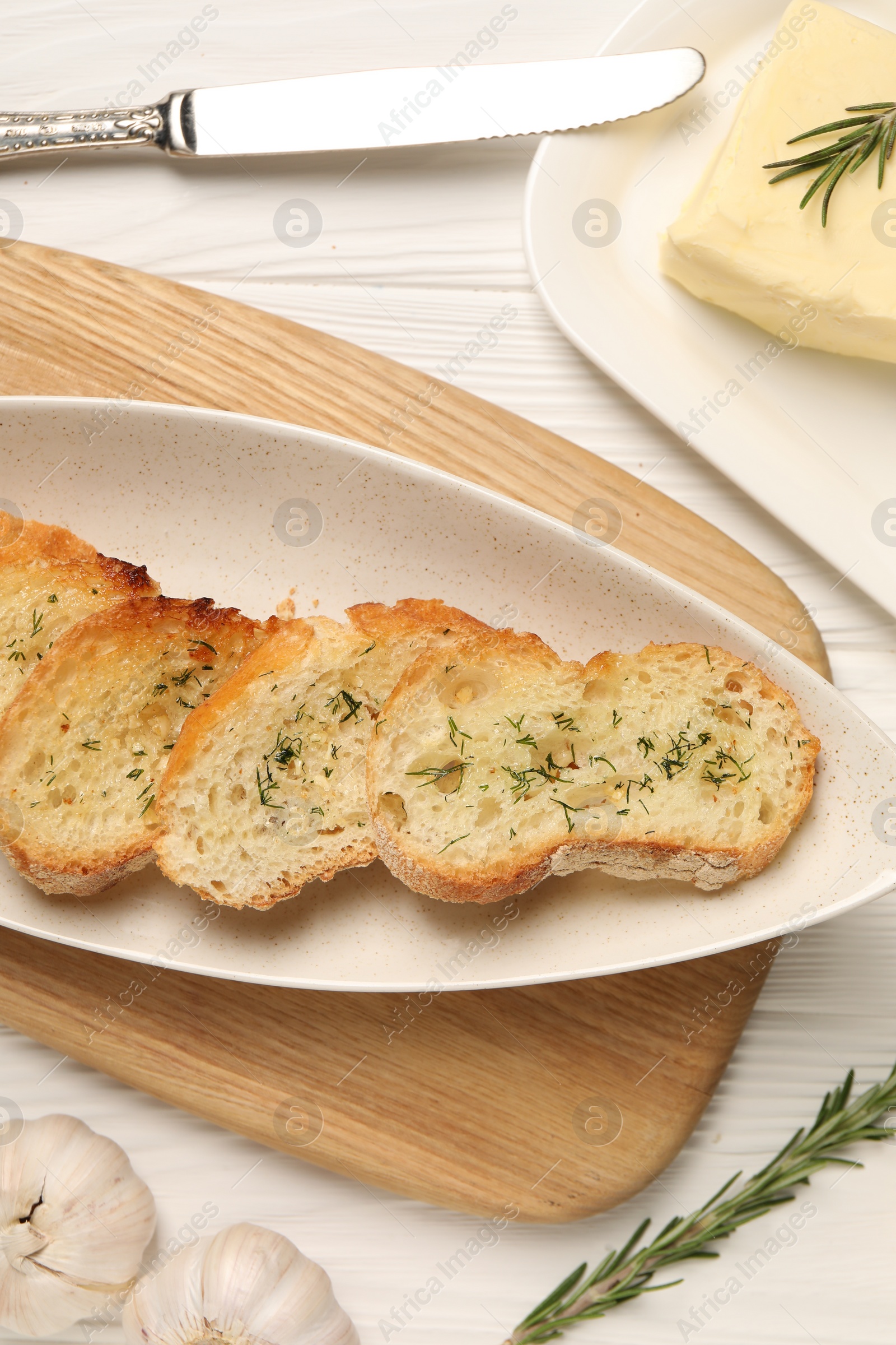 Photo of Tasty baguette with garlic and dill served on white wooden table, flat lay