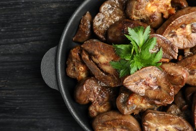 Photo of Frying pan with delicious kidneys and parsley on black wooden table, top view