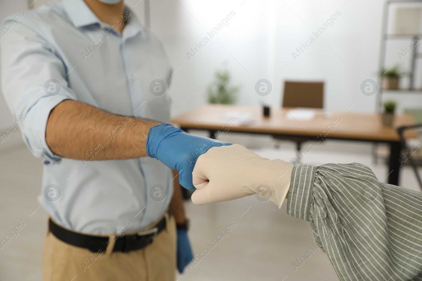 Photo of People greeting each other by bumping fists instead of handshake in office, closeup