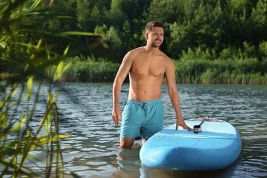 Photo of Man standing near SUP board in river water on sunny day