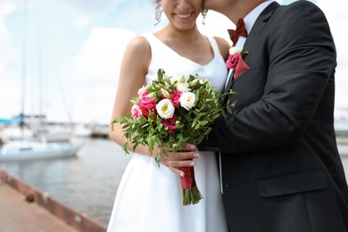 Happy newlyweds with beautiful bridal bouquet near river