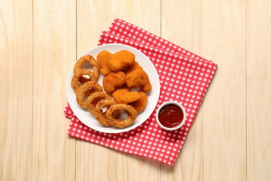 Photo of Tasty fried onion rings, chicken nuggets and ketchup on wooden table, top view