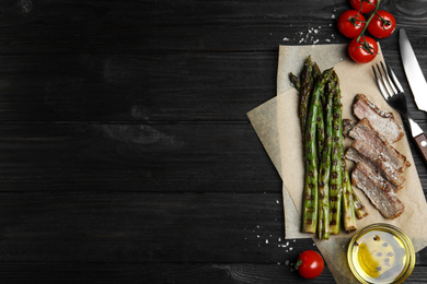 Photo of Tasty meat served with grilled asparagus on black wooden table, flat lay. Space for text