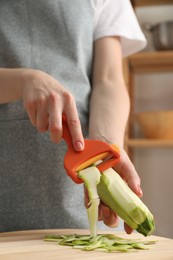 Photo of Woman peeling fresh zucchini at table indoors, closeup